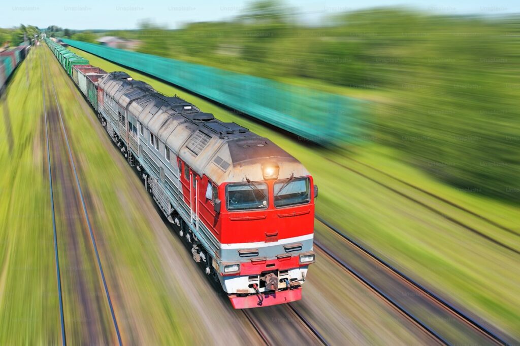 High-speed red and silver freight train moving through green countryside.