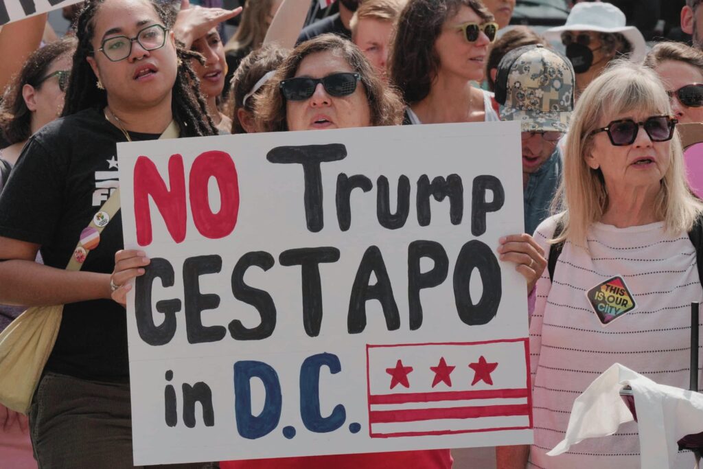A group of protesters holding a large sign reading "No Trump Gestapo in D.C." during a political demonstration.